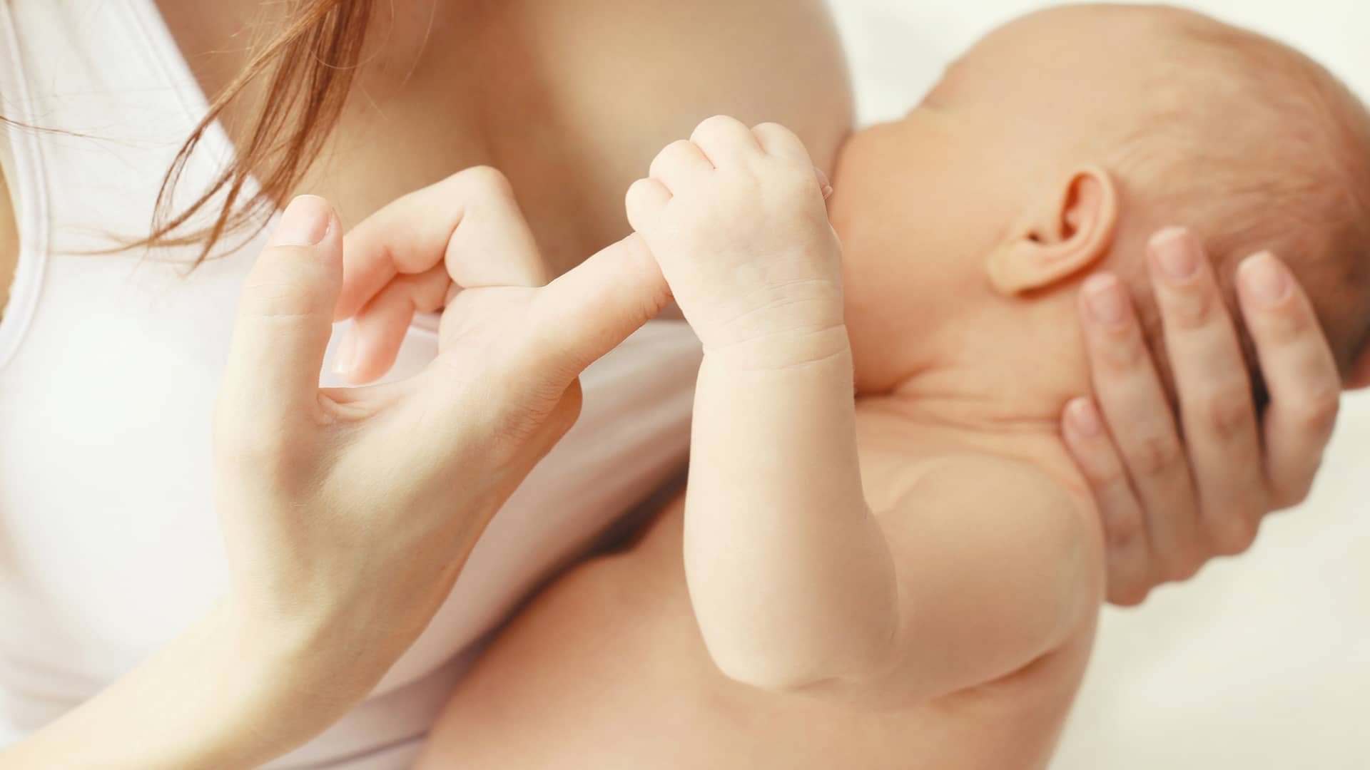Bebé agarrando fuerte el dedo de su madre porque tiene dependencia al pecho para dormir durante el periodo de lactancia materna