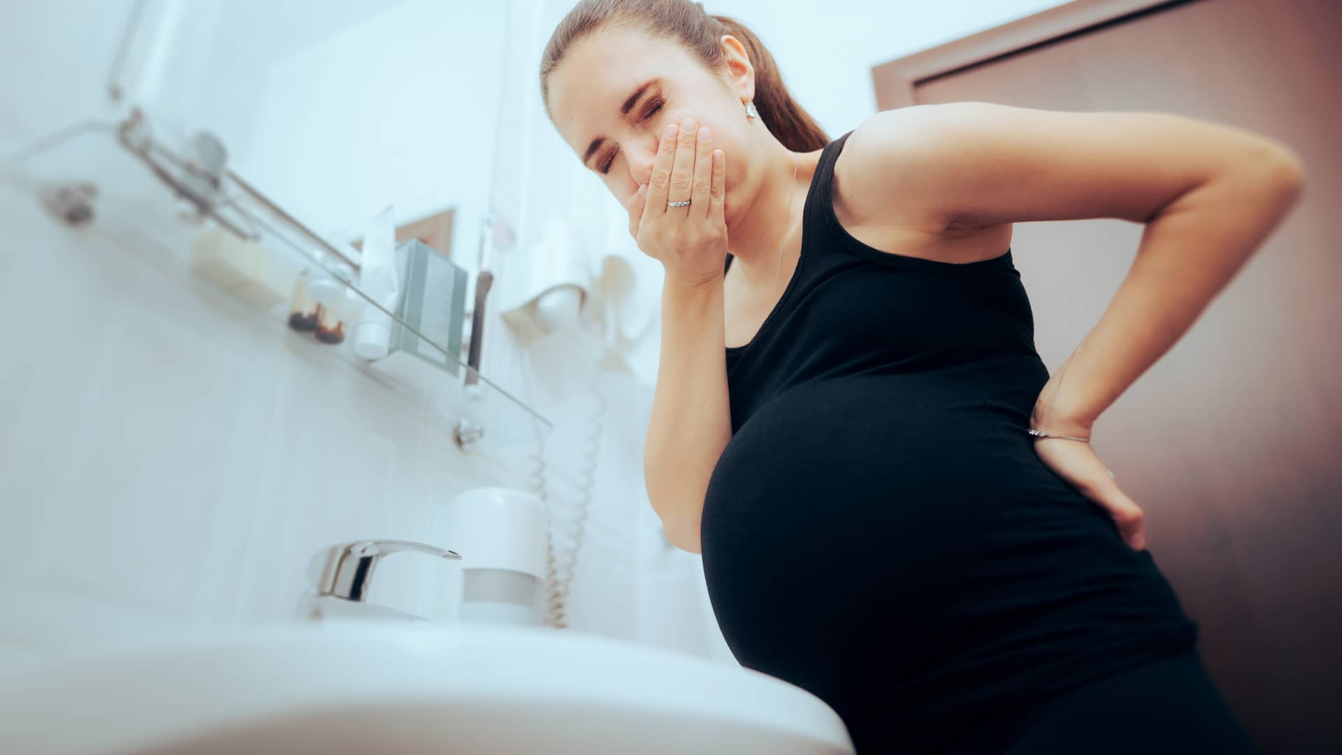 Chica tapándose la boca cerca del retrete por las nauseas que tiene en el embarazo Chica tapándose la boca cerca del retrete por las nauseas que tiene en el embarazo