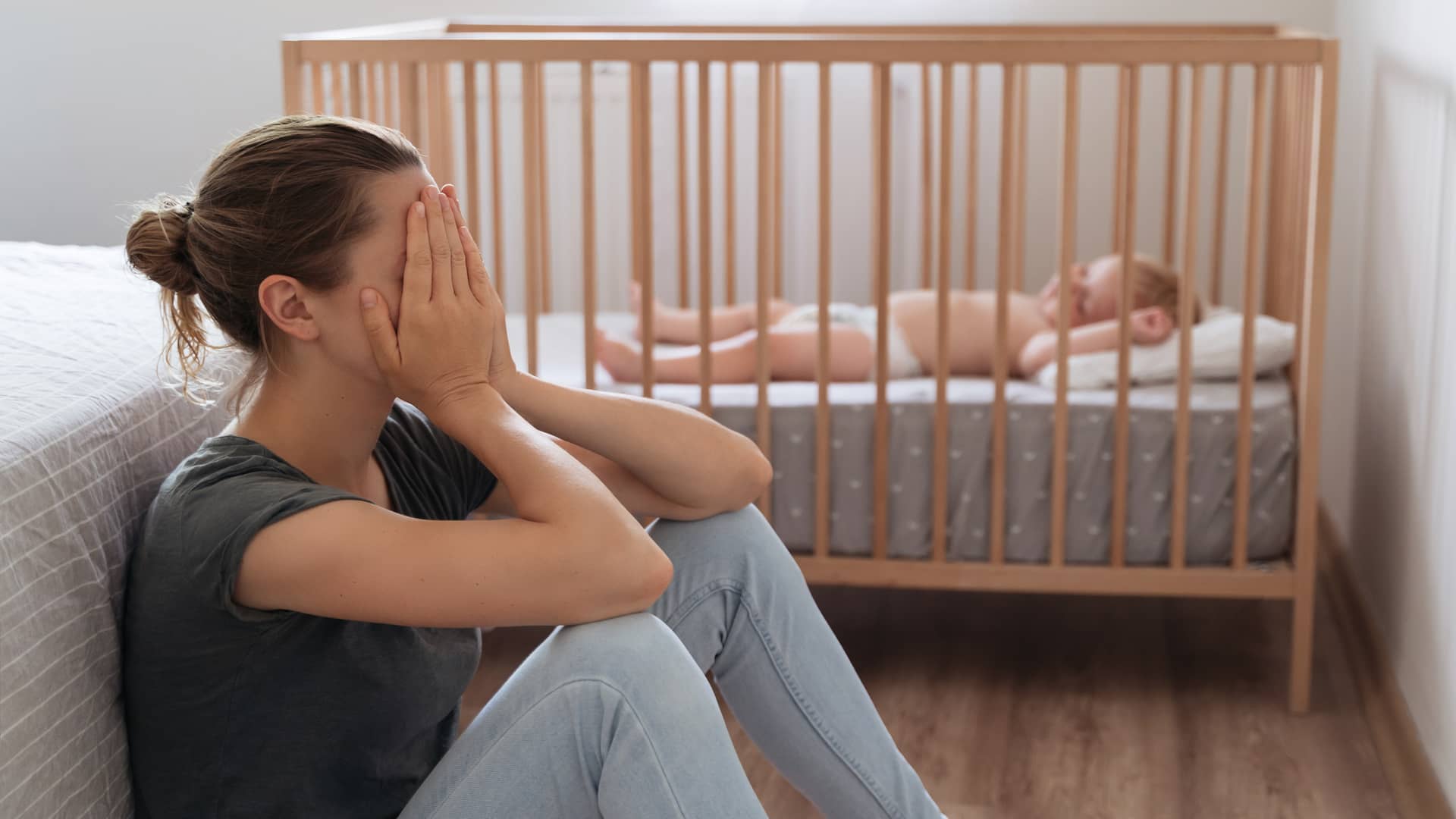 Mujer desperada con depresión postparto llorando al lado de la cuna de su bebé