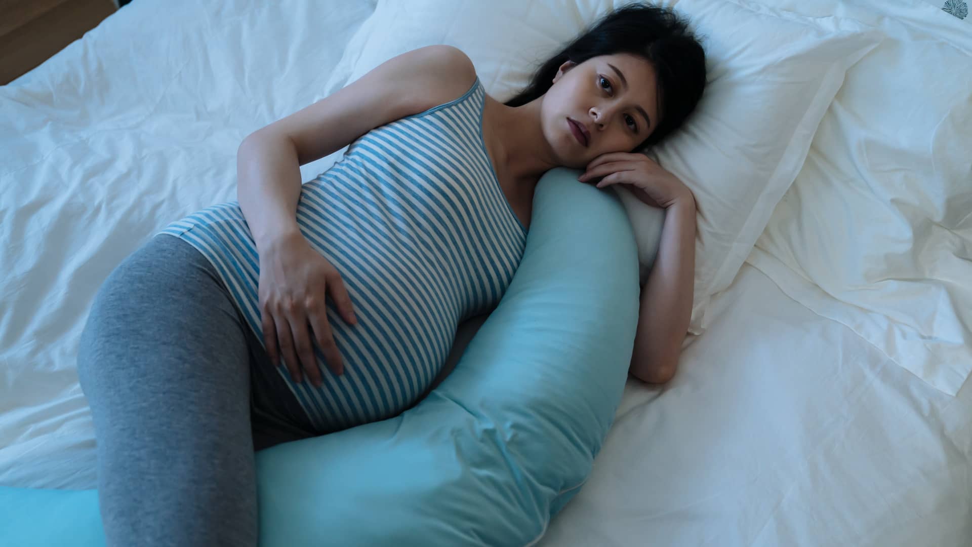 Joven embarazadas de 22 semanas tumbada en la cama consu cojín de lactancia sin poder dormir Joven embarazadas de 22 semanas tumbada en la cama consu cojín de lactancia sin poder dormir