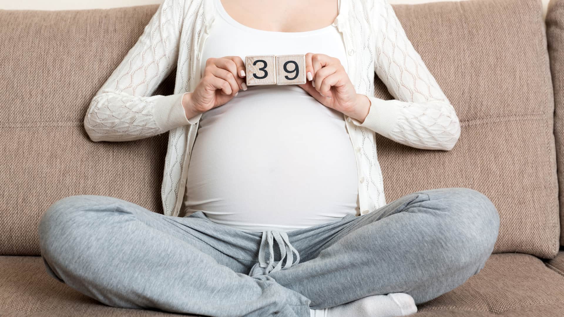 Mujer tumbada sobre la cama con unos dados de madera que indican que está en la semana 39 de embarazo