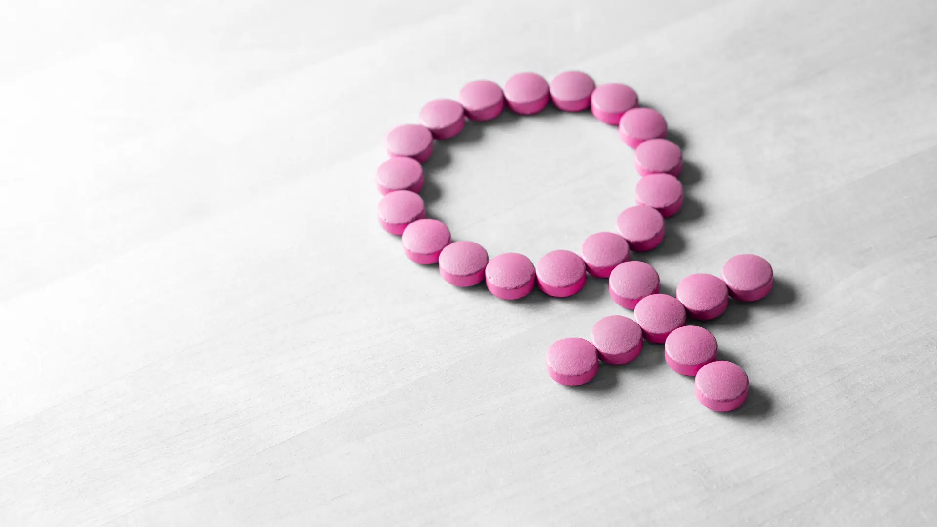 Unas pastillas rosas colcoadas en forma del simbolo de la mujer para representar los estrogenos que son una hormona sexual