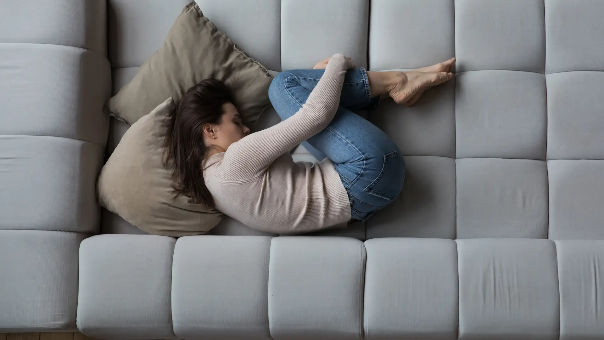 Chica dolorida en el sofa por la adenomiosis que enicma le puede provocar infertilidad