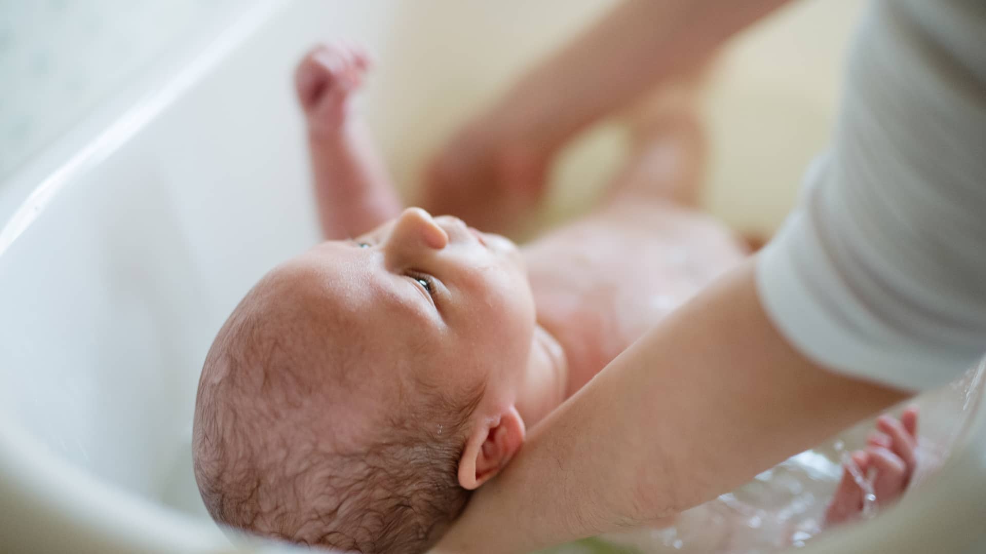 bebe muy pequeño en mitad de uno de sus primeros baños en casa por parte de sus papas