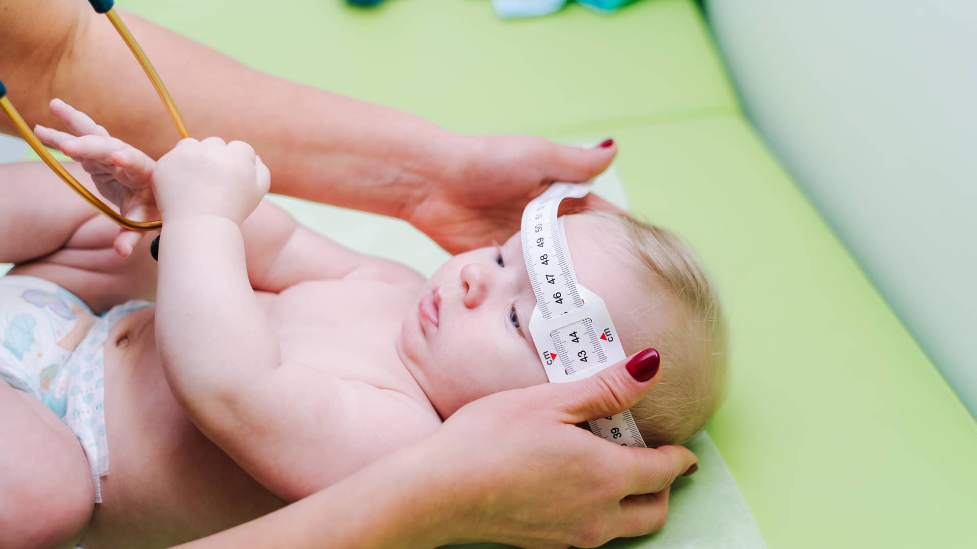 una medico midiendo el perimetro craneal de un bebe en la consulta con su metro