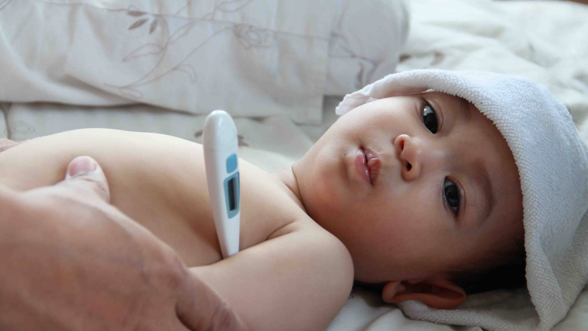 un bebe al que saben como le van a tomar la temperatura con un termometro digital en la axila