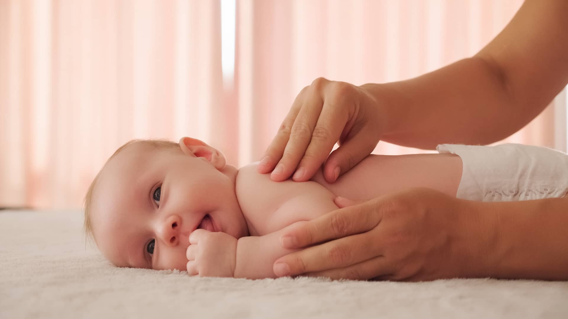 bebe de 6 meses tumbado boca abajo mientras su mama le echa crema en la espalda