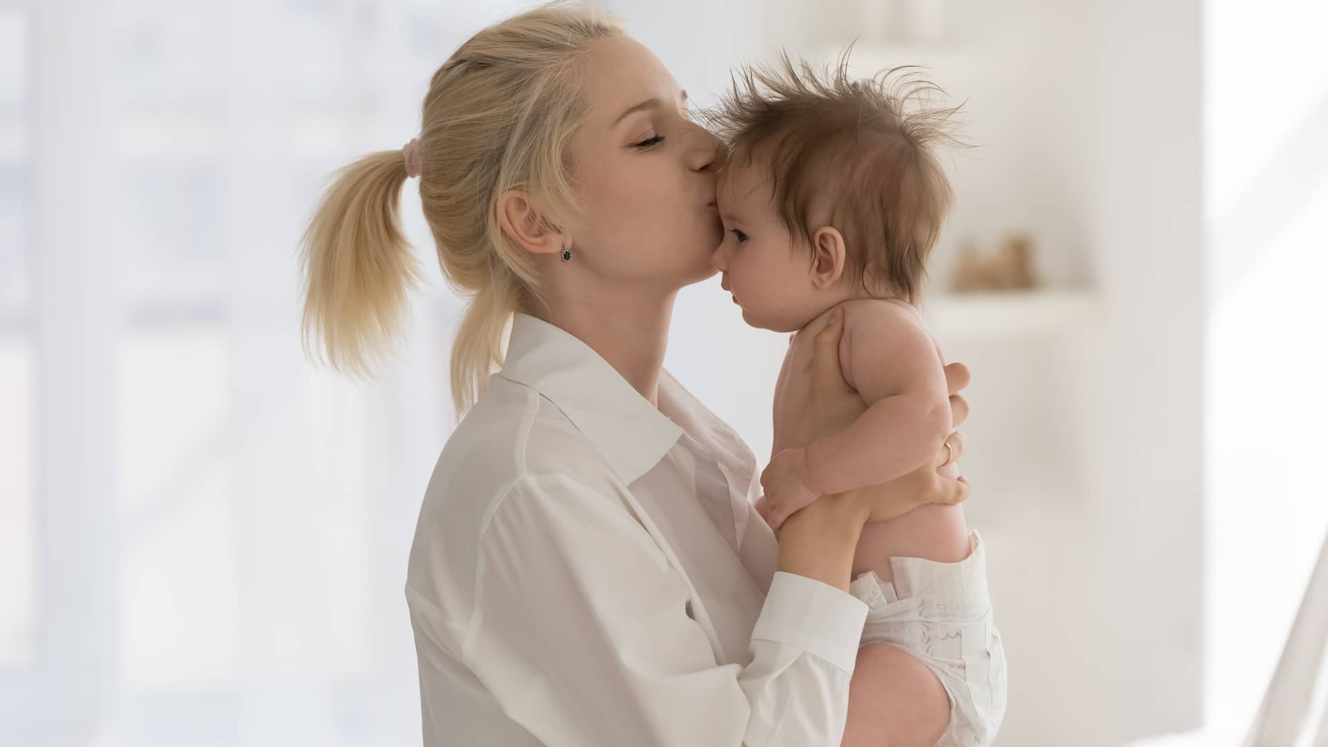 mama besando a su bebe de 8 meses en la frente despues de cambiarle el pañal