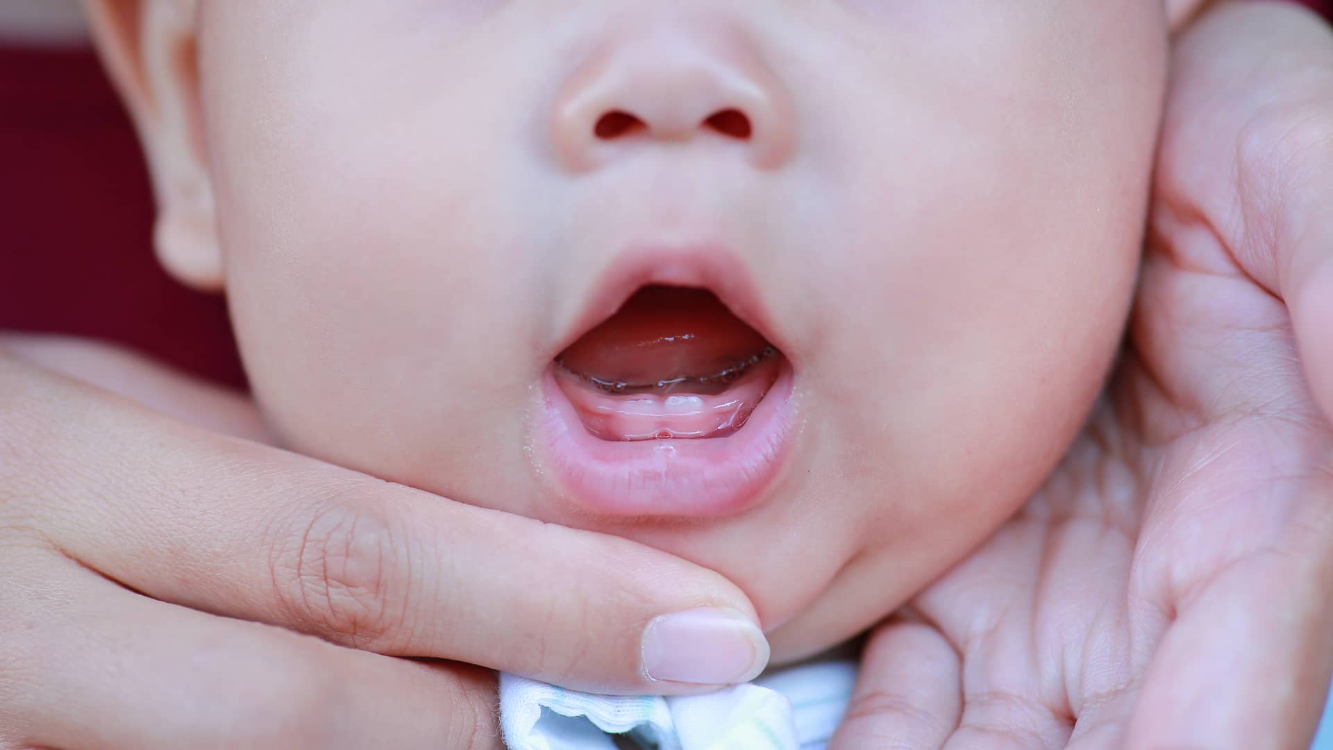 Mamá de un bebé abriéndole la boca un poco para que se vean sus primeros dientes