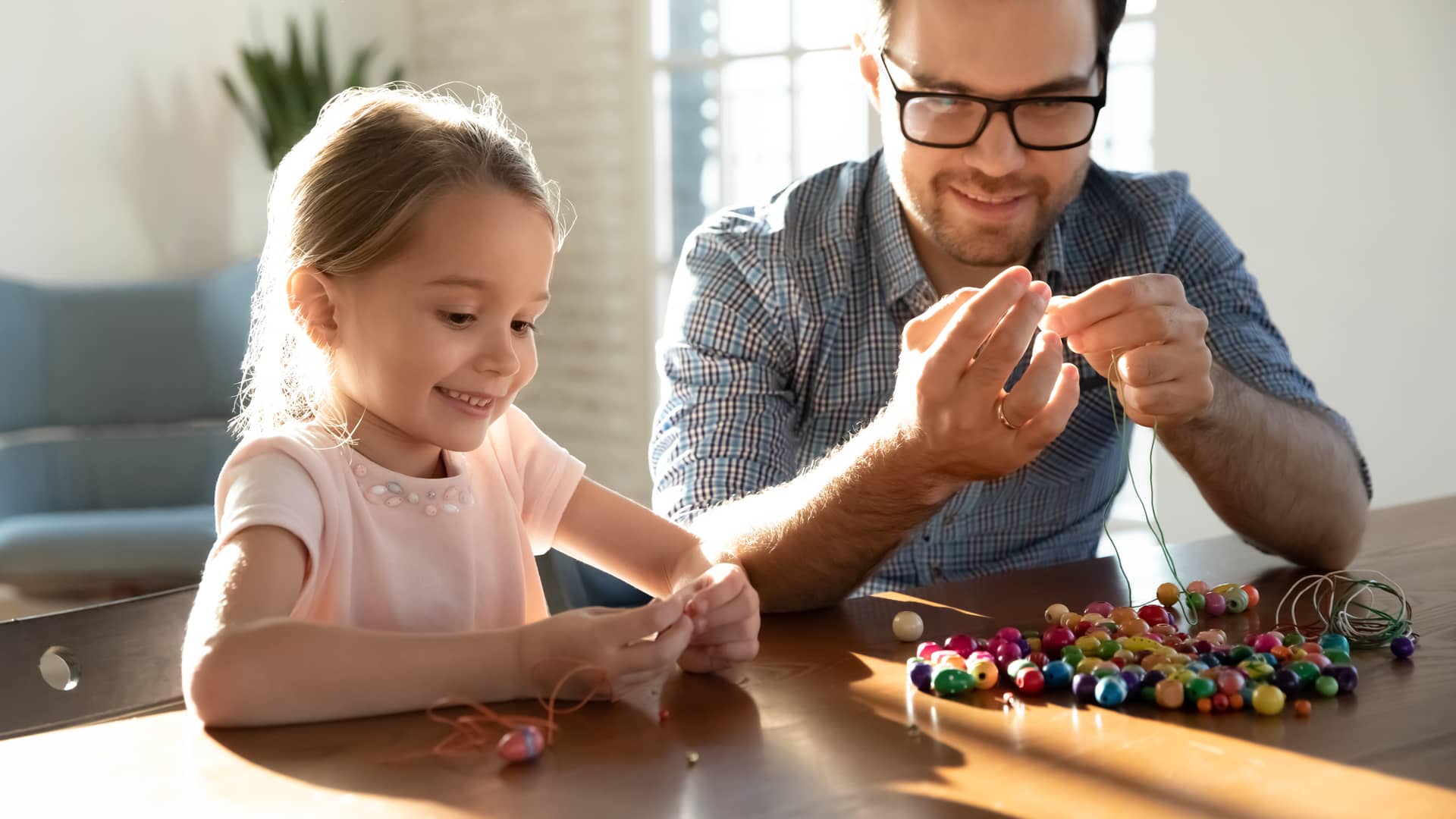 Una niña de 4 años haciendo pulseras de abalorios grandes de madera con su padre para su estimulación temprana