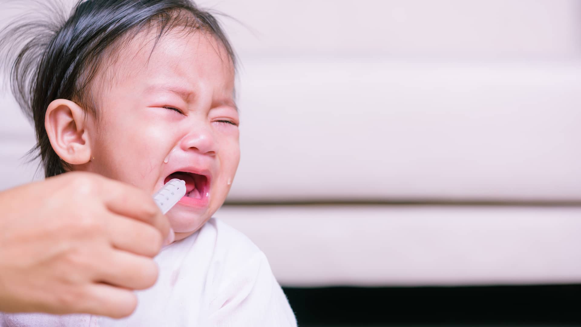 bebe llorando mientras su madre le intenta dar la amoxicila en jarabe espeical para niños