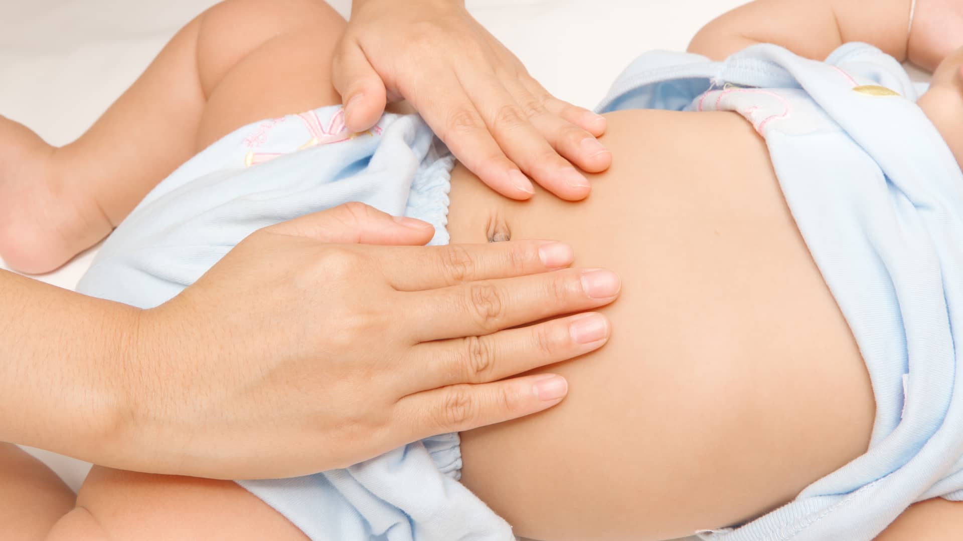 manos de una mama dando un masaje en la tripa a su bebe que se llora por el dolor que le produce la celiaquia