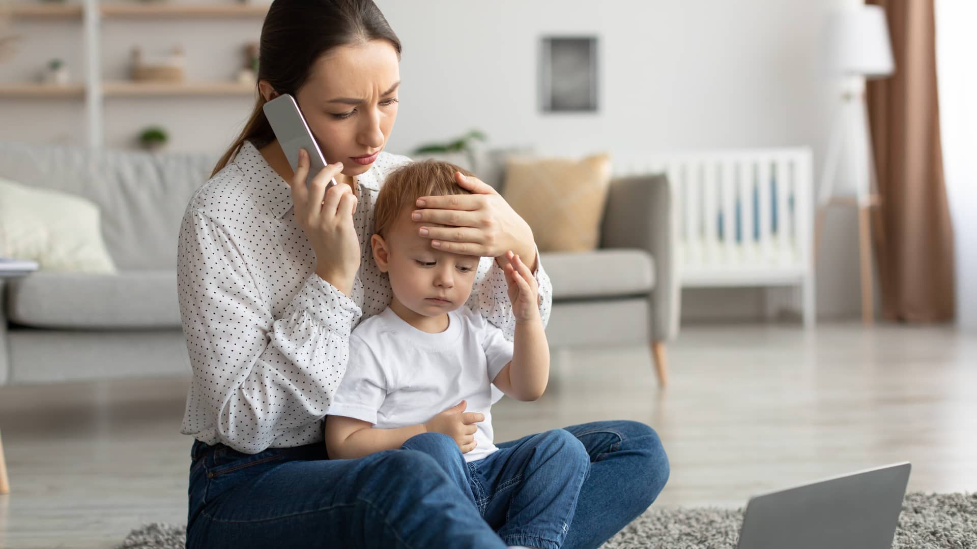 una mama mirando si su hijo tiene fiebre mientras llama a la pediatra para que atienda a su bebe con infeccion de orina