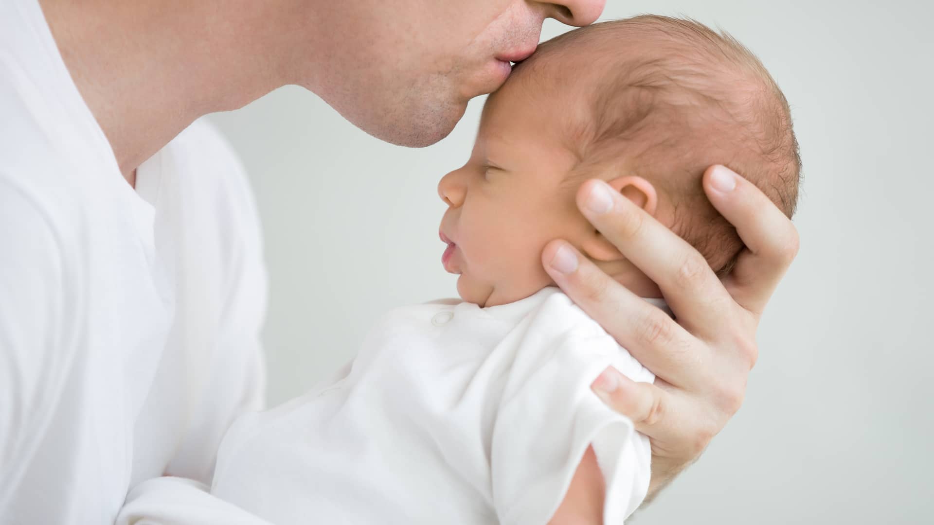 un papa agarrando a su bebe por la cabeza con microcefalia mientras le besa en la frente un papa agarrando a su bebe por la cabeza con microcefalia mientras le besa en la frente