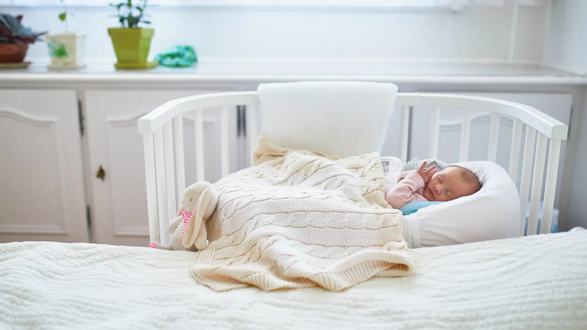 Una cuna de colecho al lado de una cama de un matrimonio que es un método de sueño en bebés